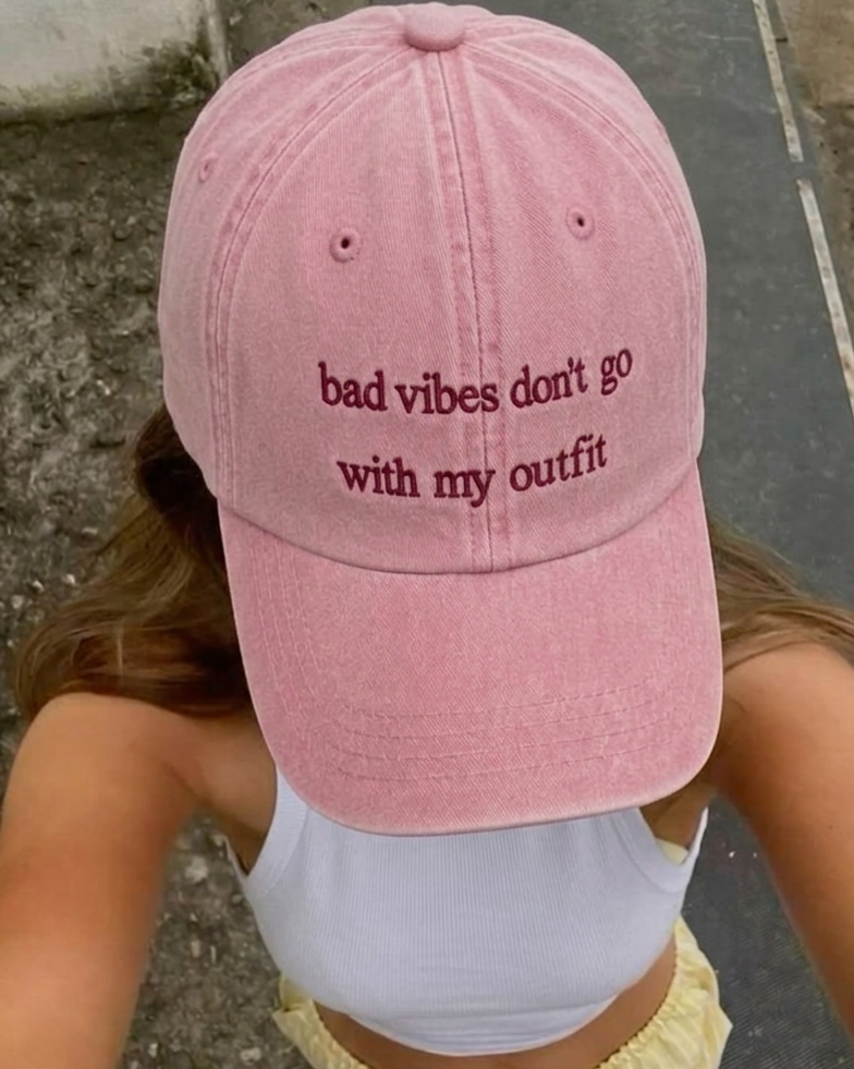 Pink cap with 'bad vibes don't go with my outfit' text worn by a person.
