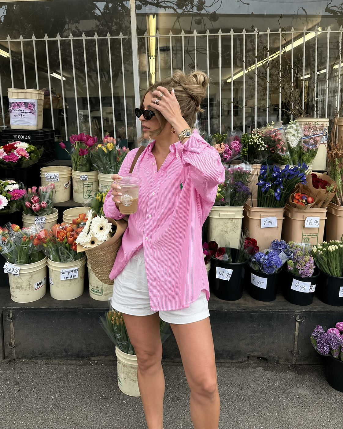 Woman in pink shirt and white shorts standing in front of a flower stand.