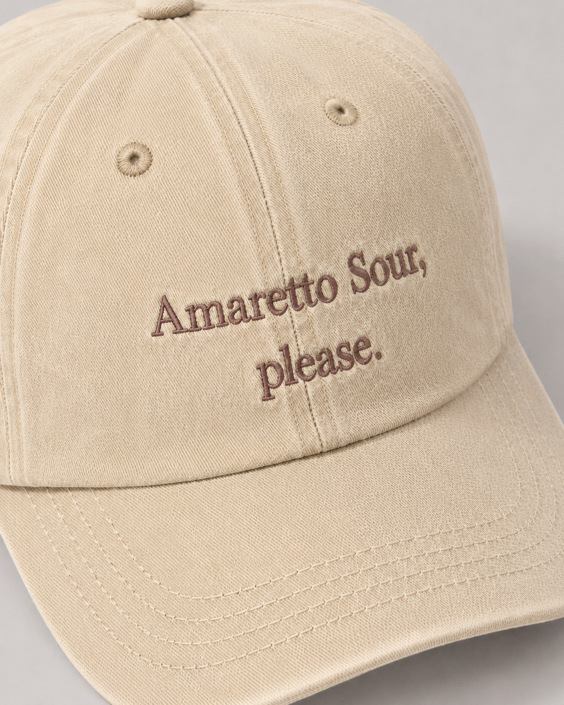 Beige cap with 'Amaretto Sour, please.' text on a gray background