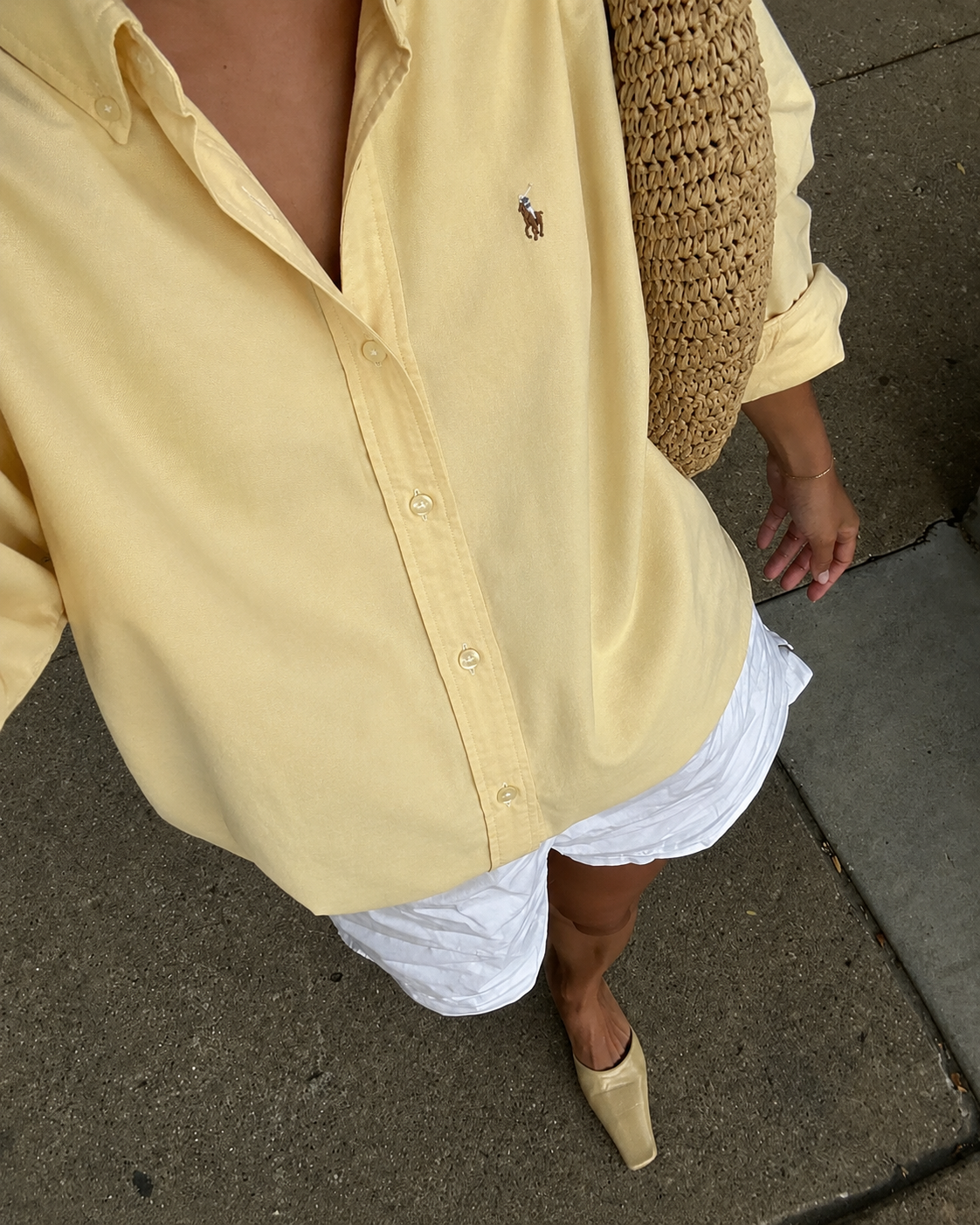 Person wearing a yellow shirt with a brand logo and white pants on a sidewalk.