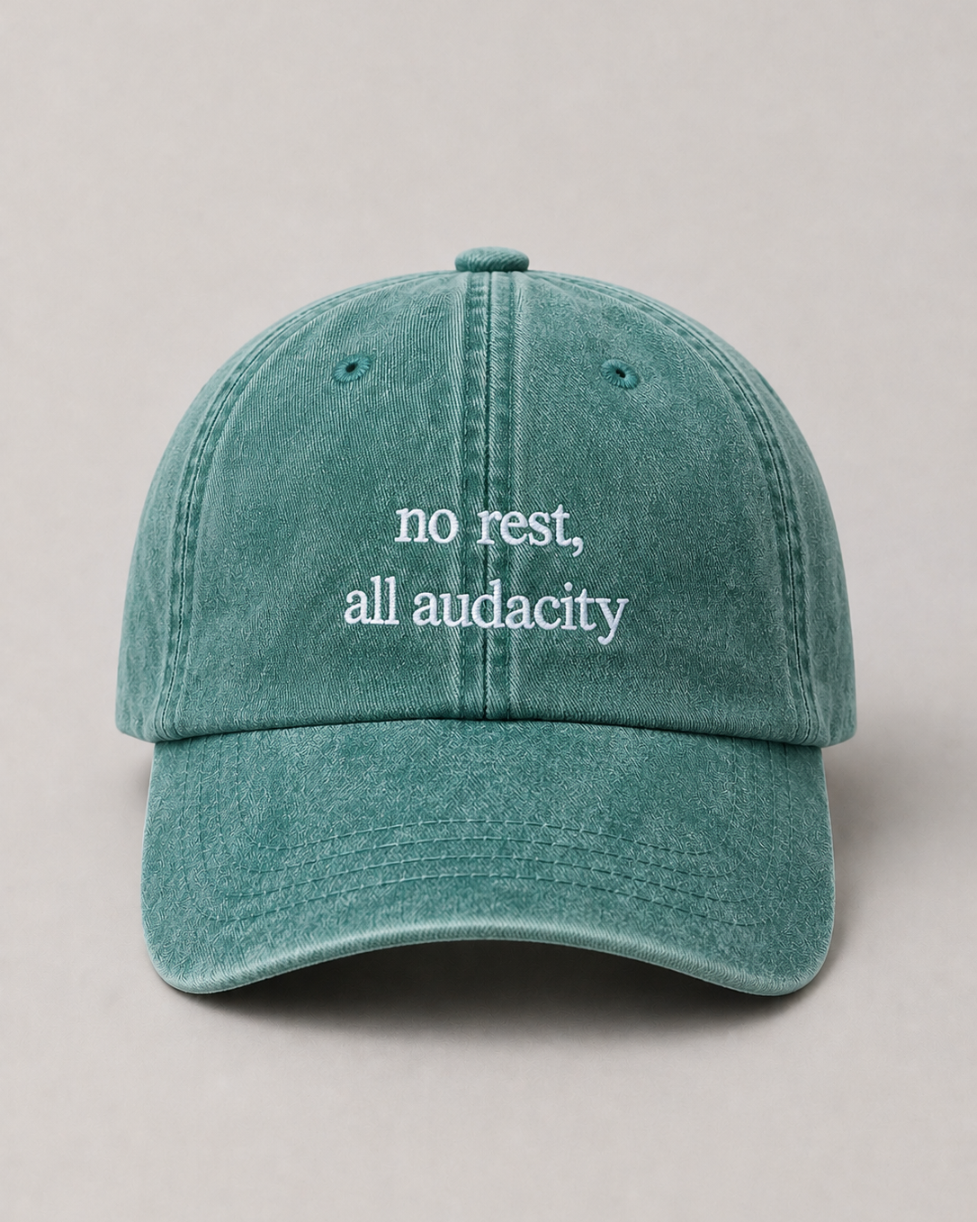 Teal cap with 'no rest, all audacity' text on a beige background