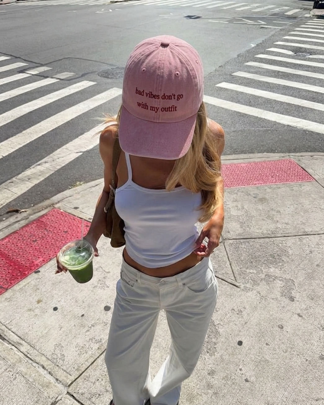Person wearing a pink cap with text, white top, and light jeans on a city street.