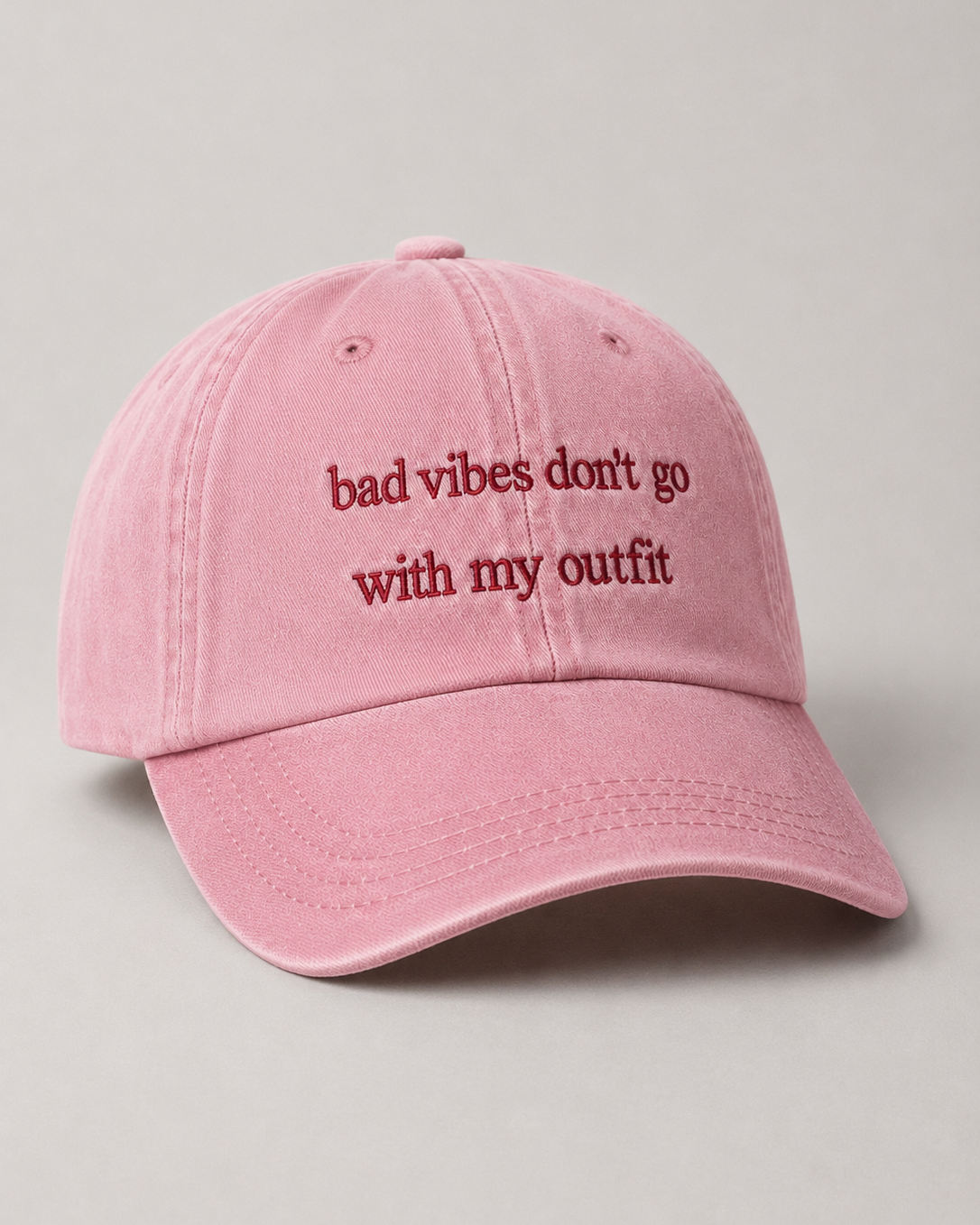 Pink cap with text 'bad vibes don't go with my outfit' on a light gray background