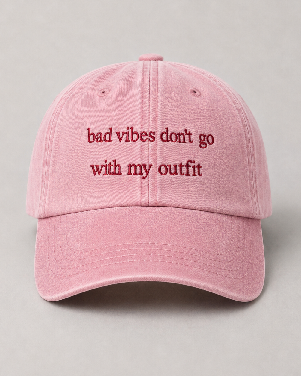 Pink cap with text 'bad vibes don't go with my outfit' on a gray background