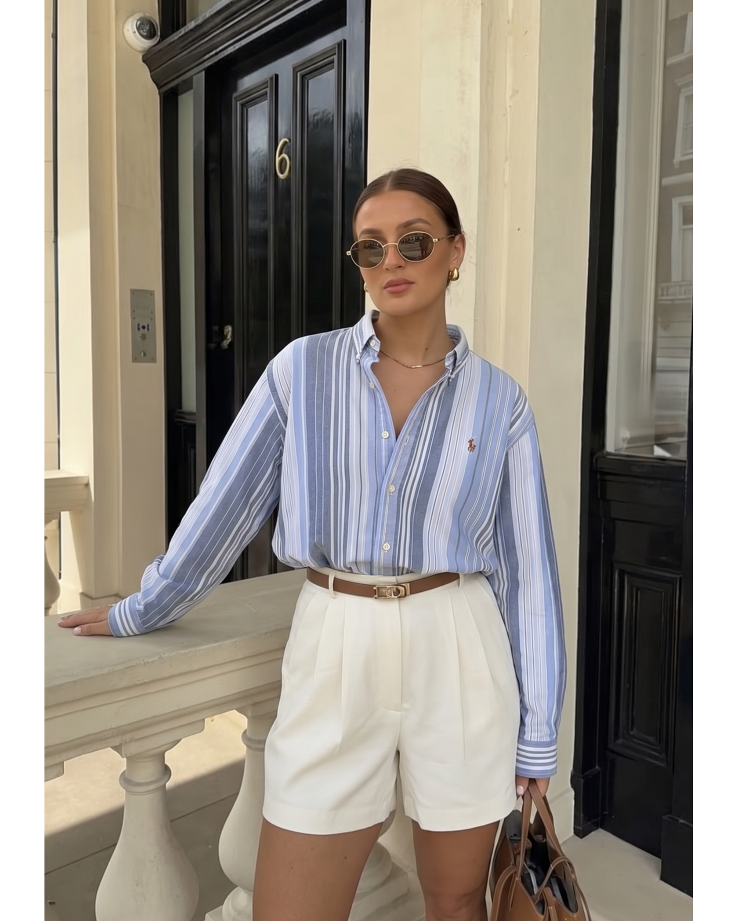 Woman wearing a striped shirt and white shorts standing on a balcony.