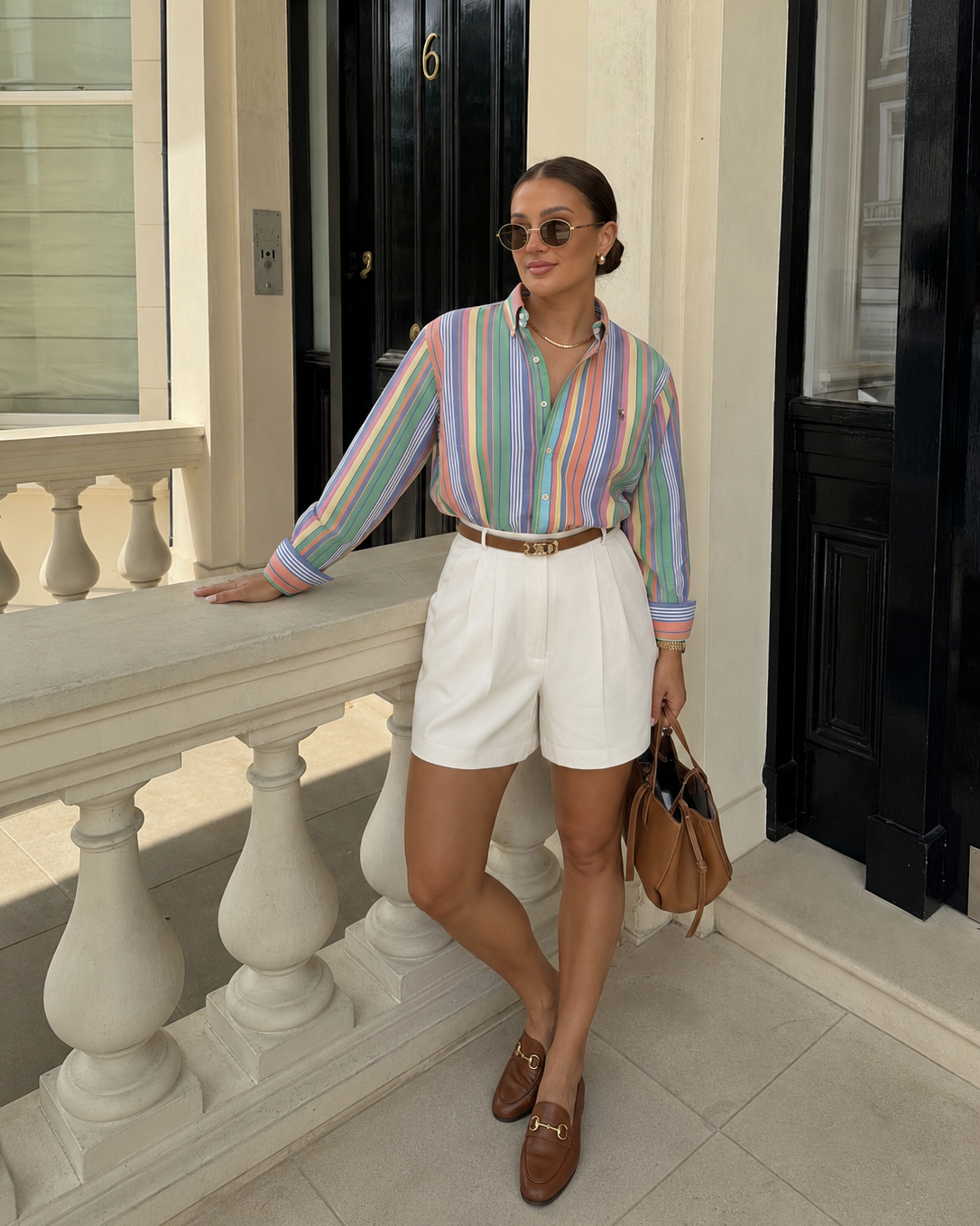 Woman in colorful striped shirt and white shorts standing on a balcony.