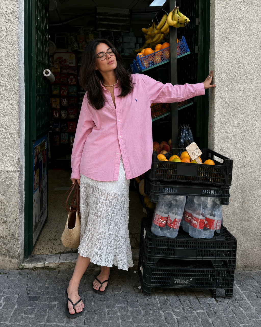 Woman in pink shirt standing next to a fruit stand with water bottles and crates.
