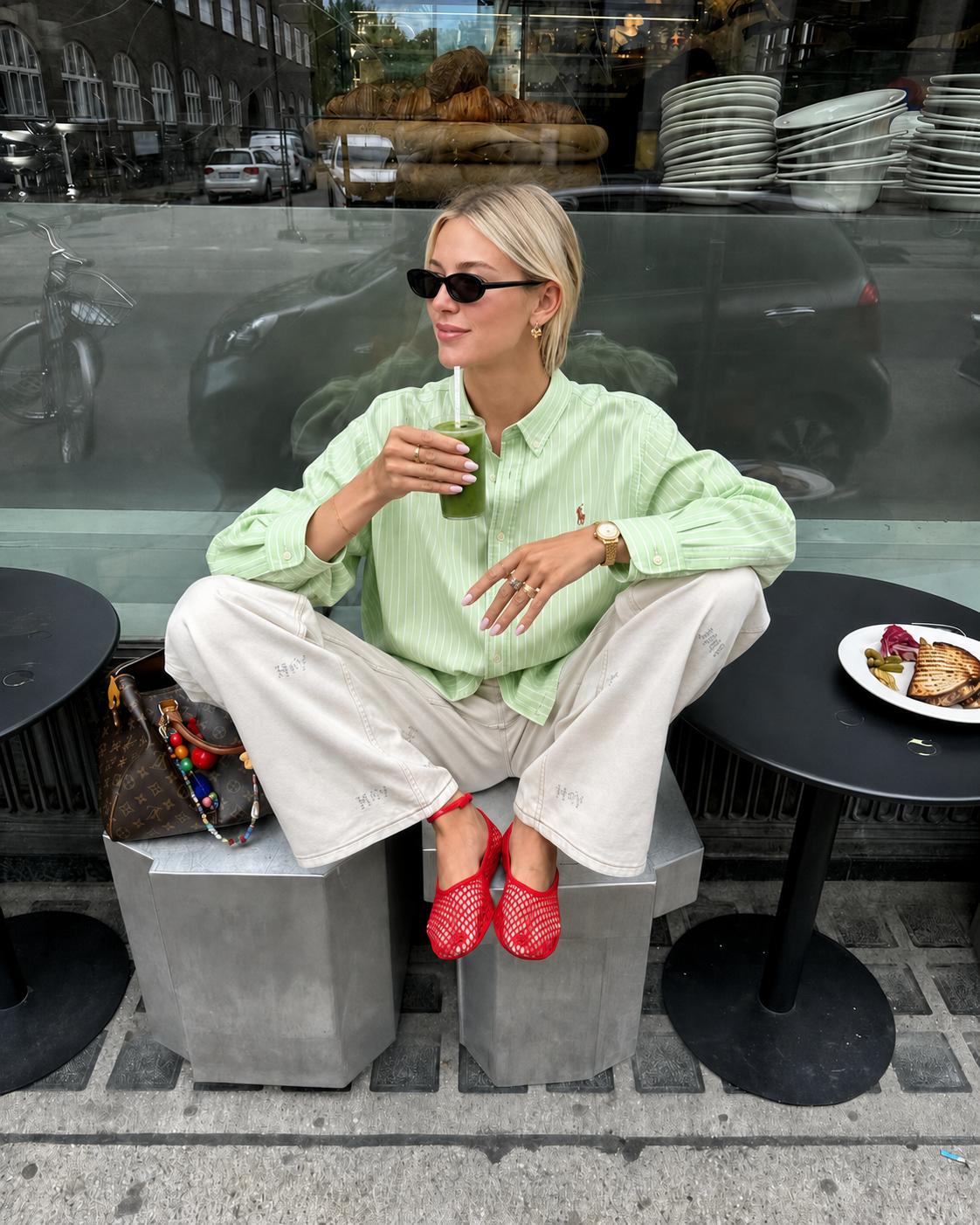 Woman in a light green shirt and red shoes sitting on a concrete block, drinking from a green cup.
