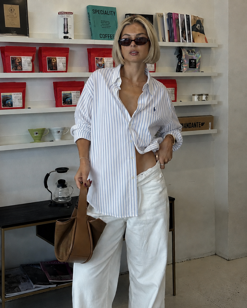 Woman in a casual outfit with a striped shirt and white pants standing in a room with shelves.