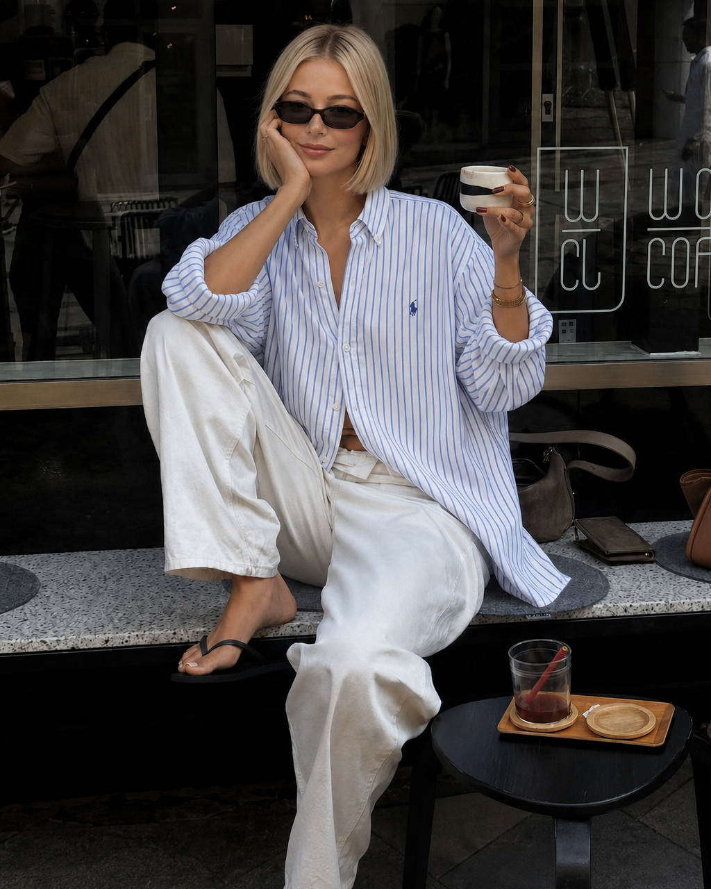 Woman sitting on a bench holding a coffee cup in front of a store window.
