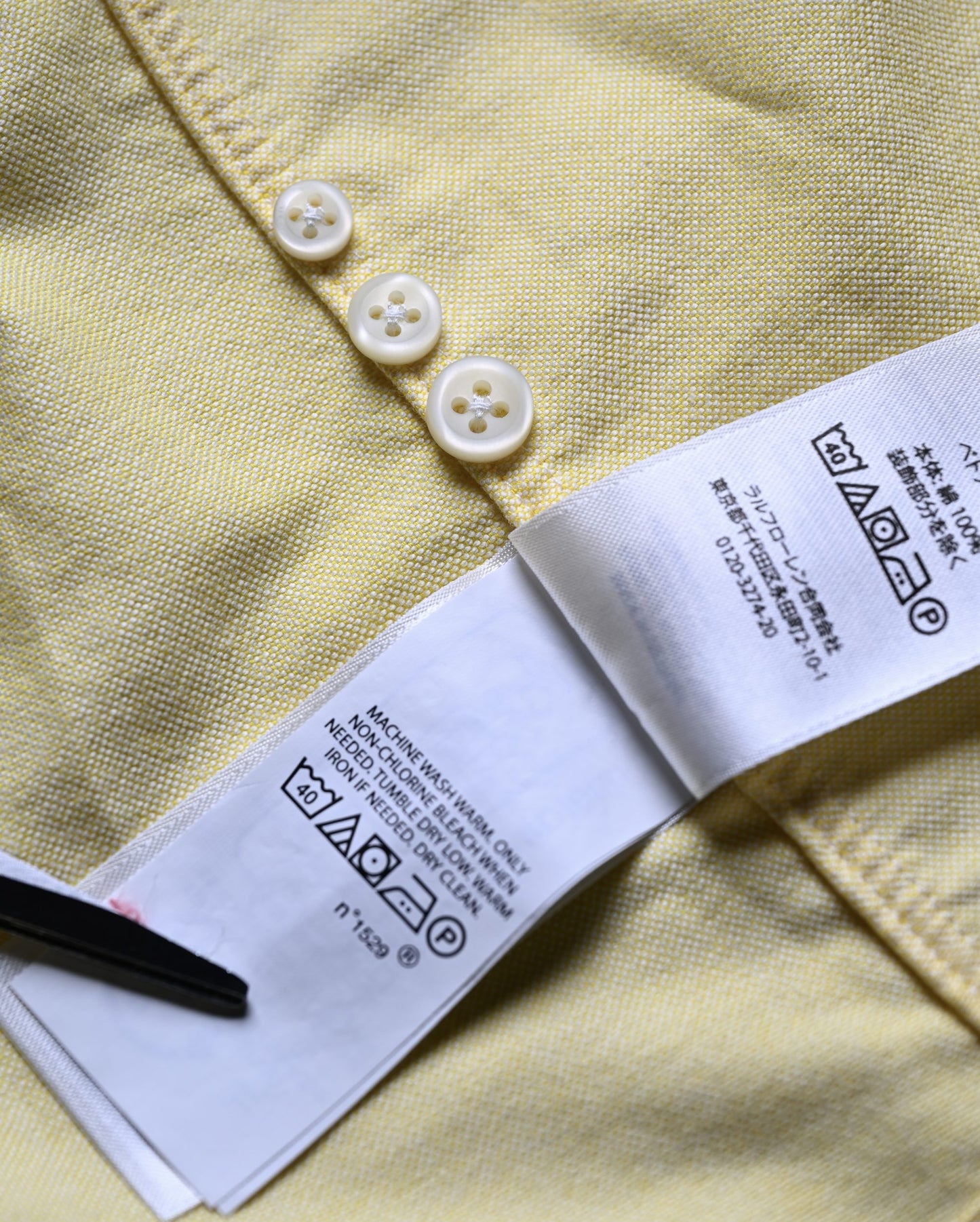 Close-up of a yellow shirt with buttons and a Ralph Lauren label custom fit vintage shirt label size large on a matching fabric background.  Soft cotton fabric detail of vintage Ralph Lauren oxford shirt