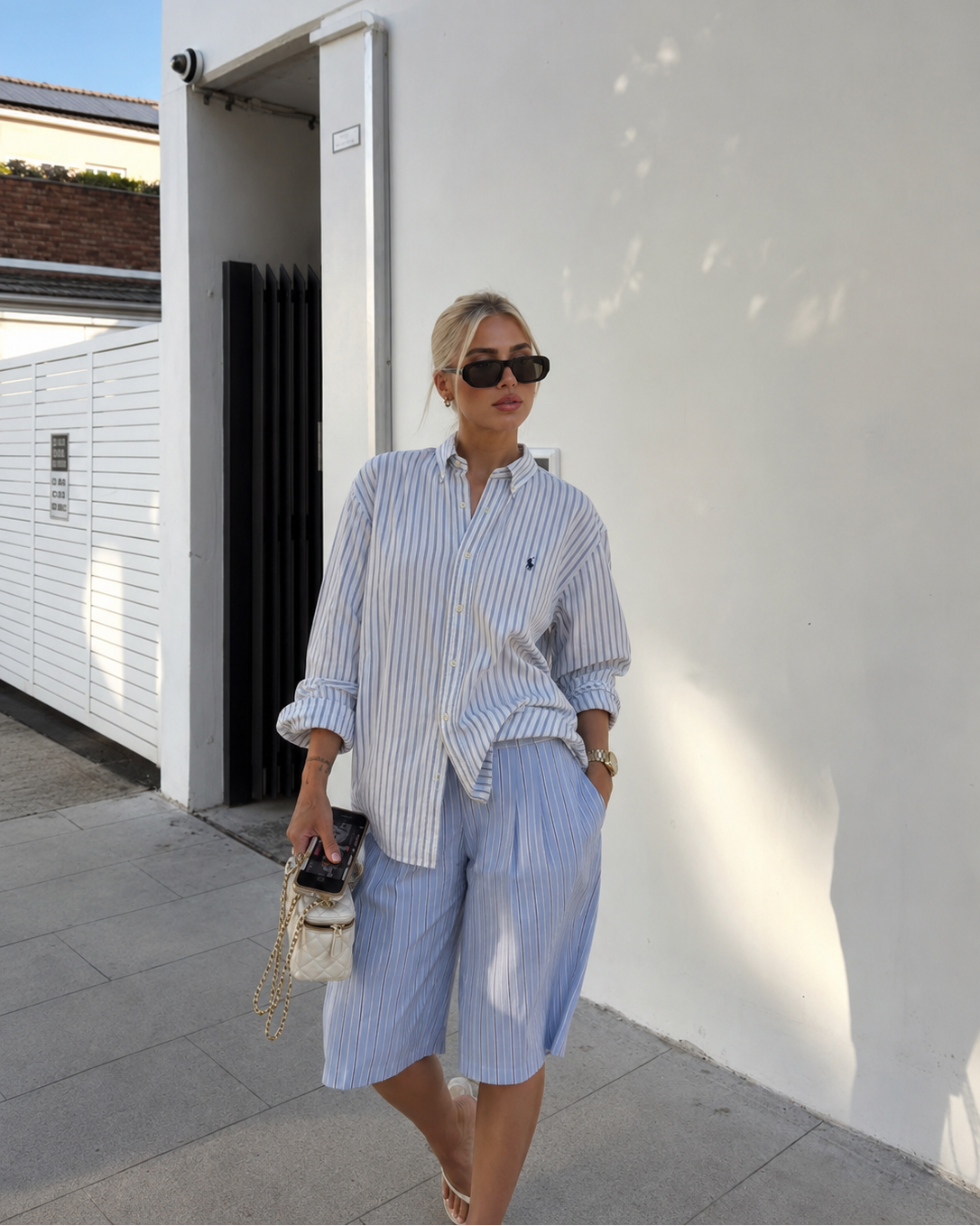 Woman in a blue and white striped shirt and shorts standing against a white wall.